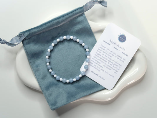 Blue beaded bracelet on a blue drawstring bag with blue bracelet and a card on a white surface